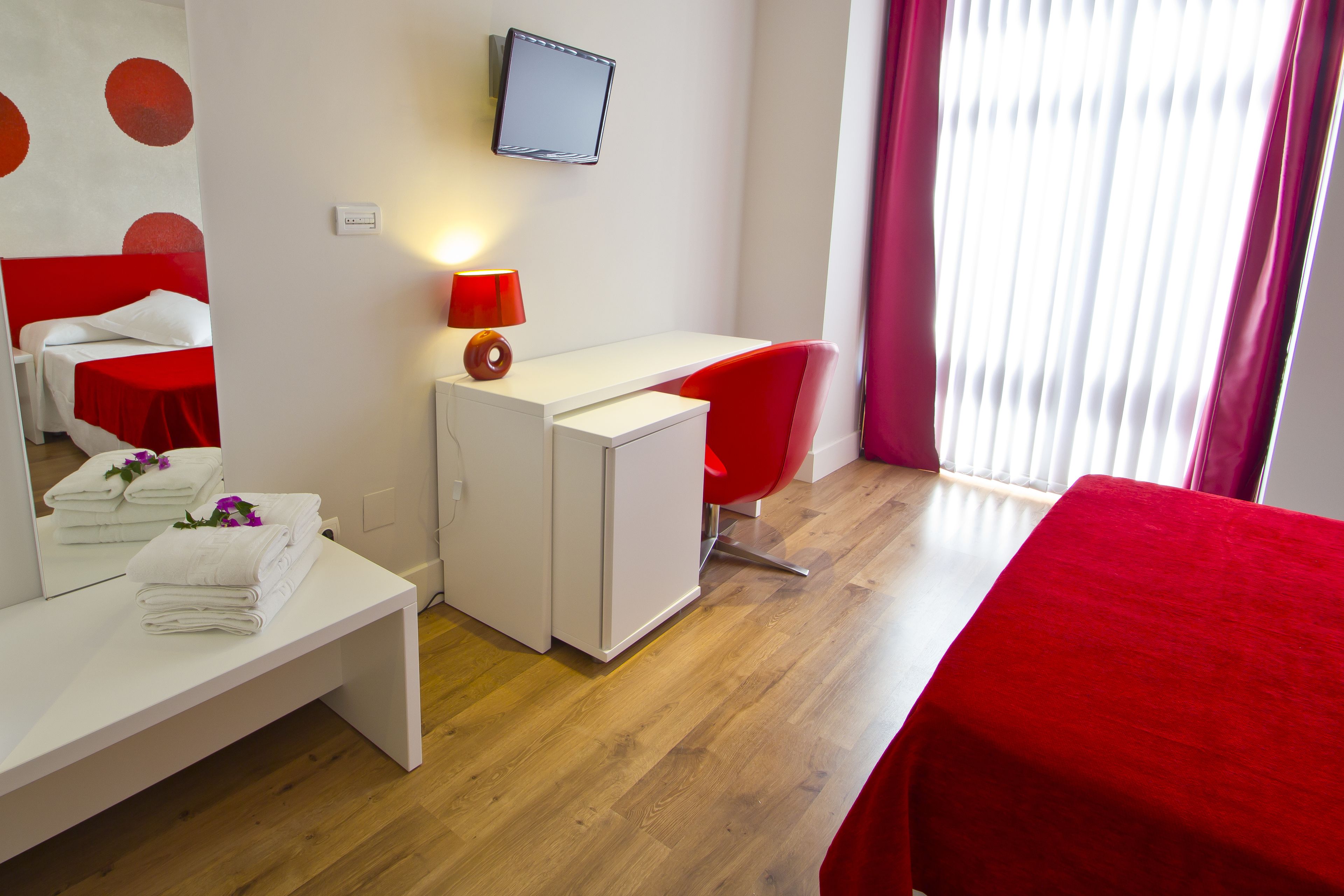 Een hotelkamer met een bed, een bureau, een stoel, een televisie en een raam met gordijnen.