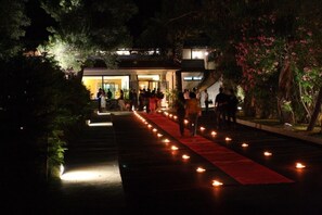 A nighttime outdoor event with a red carpet and lit candles.