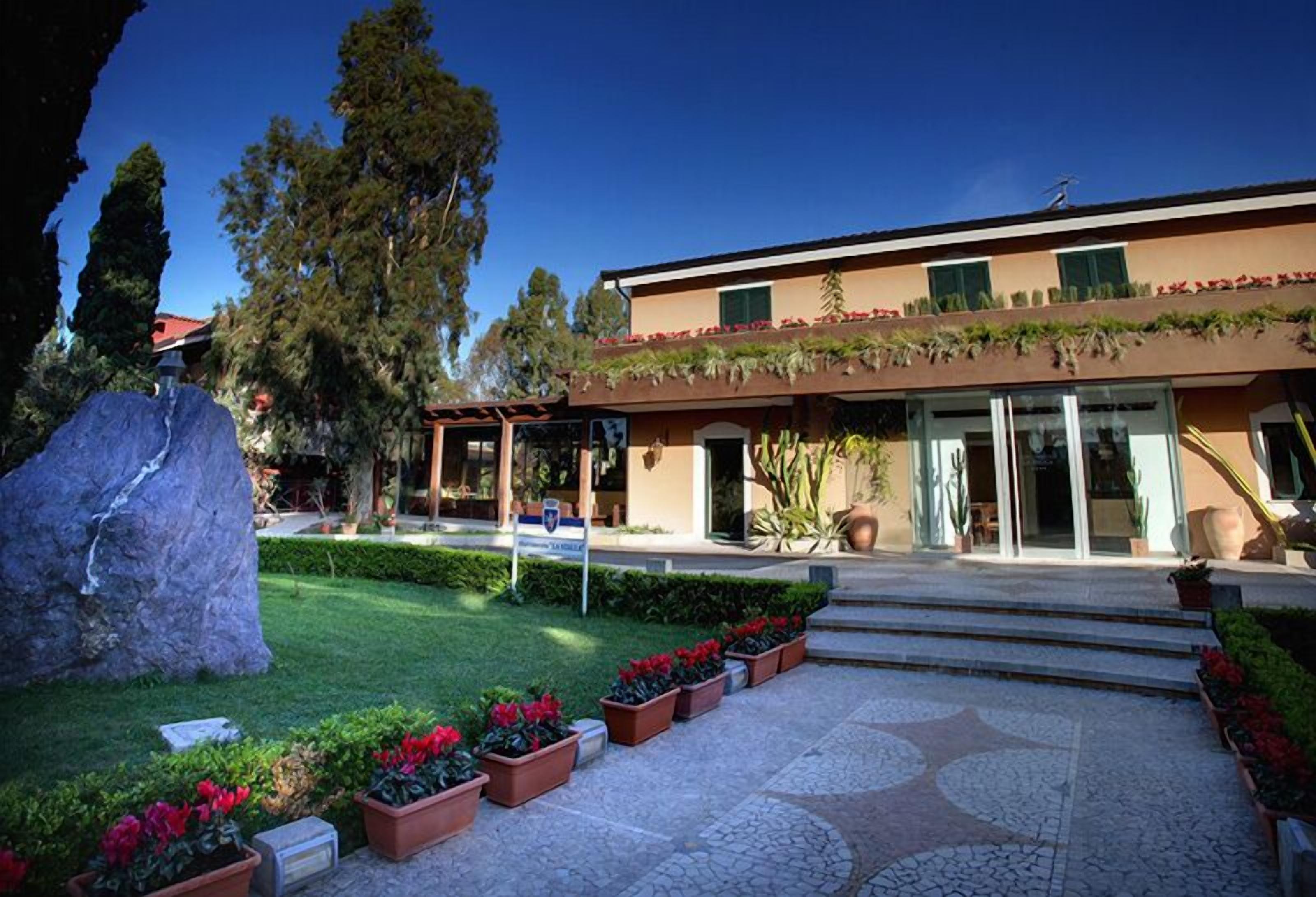 A modern building with a flat roof, large windows, and a stone pathway leading to the entrance.