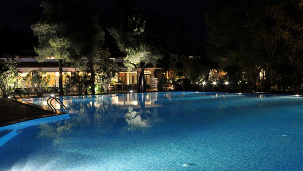 A nighttime swimming pool with surrounding trees and a building with illuminated windows. - La Bruca Resort (Scalea)