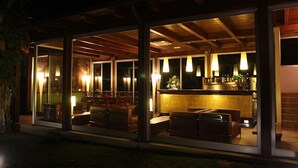 A modern outdoor seating area with glass walls, wooden beams, and ambient lighting. - La Bruca Resort (Scalea)