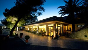 A well-lit building with a covered outdoor area, possibly a restaurant or cafe, with a paved entrance and potted plants. - La Bruca Resort (Scalea)