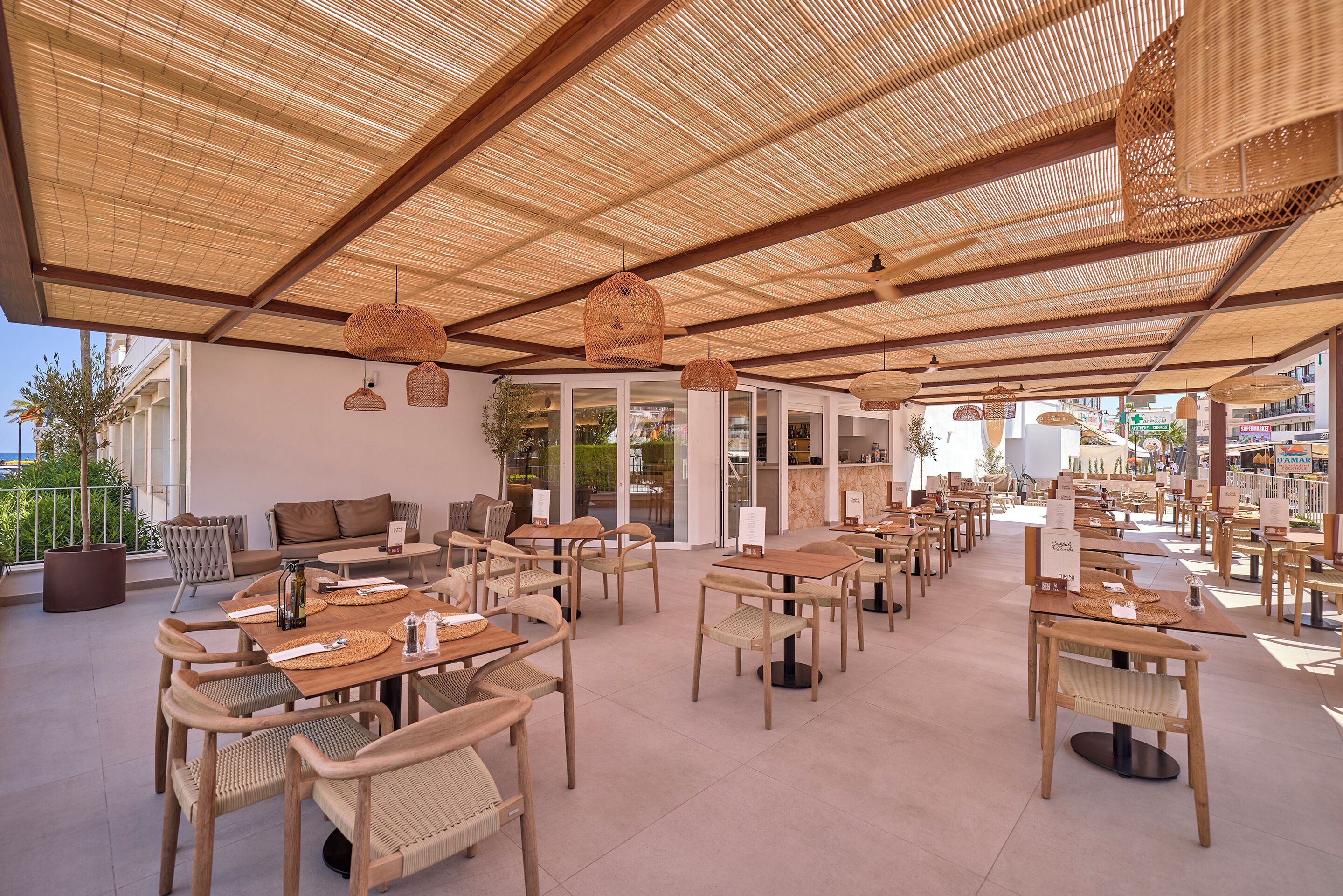 An outdoor cafe with wicker furniture and a thatched roof.