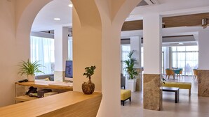 A modern reception area with a wooden desk, a computer, and two potted plants. - Universal Hotel Bikini (Sant Llorenc des Cardassar)