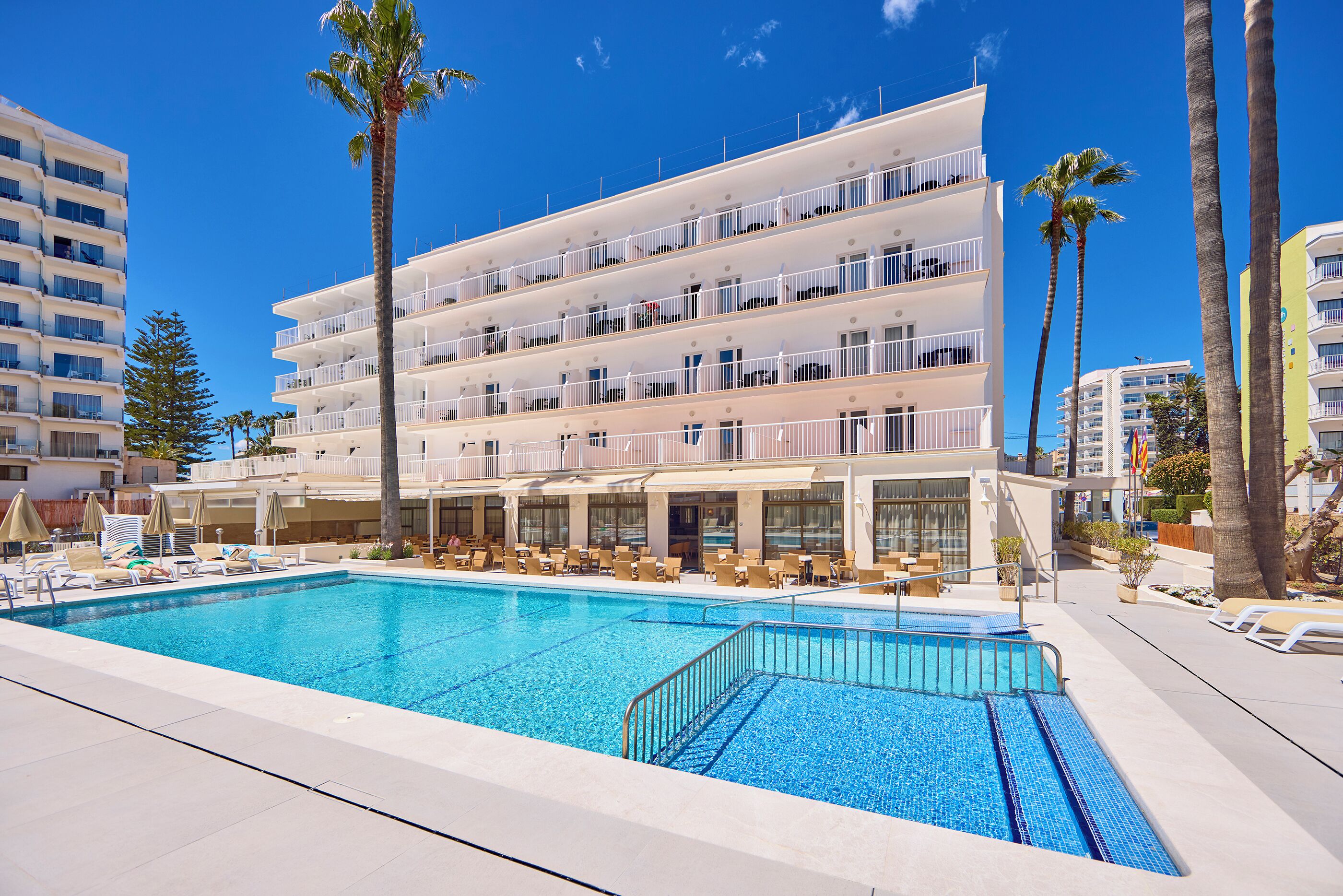 A hotel with a pool, multiple balconies, and palm trees.