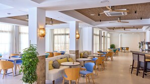 A spacious hotel lobby with a mix of seating areas, including sofas and round tables, and a central bar area. - Universal Hotel Bikini (Sant Llorenc des Cardassar)