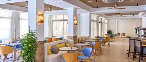 Eine großzügige Hotelhalle mit verschiedenen Sitzbereichen, darunter Sofas und runde Tische, sowie einer Bar in der Mitte.