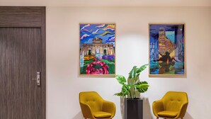 A room with two yellow chairs, a large potted plant, and two colorful paintings on the wall.