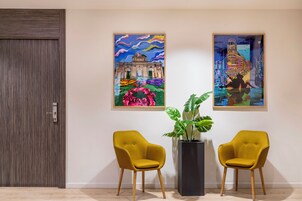 A room with two yellow chairs, a large potted plant, and two colorful paintings on the wall.