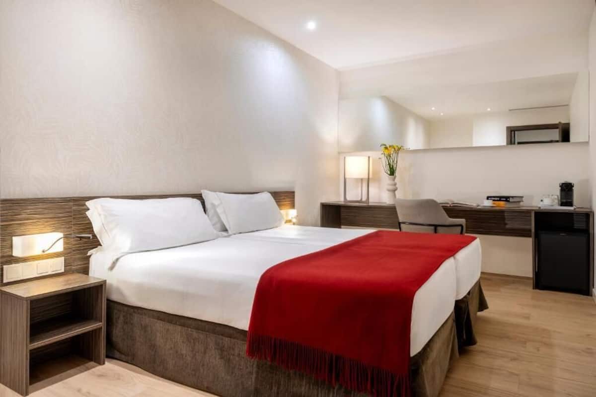 Una habitación de hotel moderna con una cama grande, mesitas de noche, un escritorio y una silla.