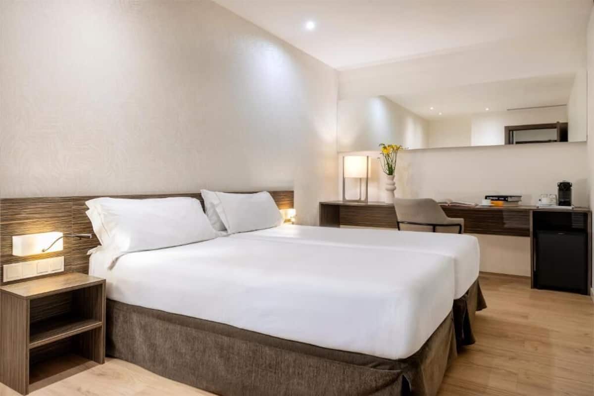 Habitación de hotel con una cama grande, mesitas de noche, un escritorio y una silla.