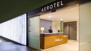 An Aerotel hotel reception area with a wooden reception desk, a receptionist, and a modern interior design.