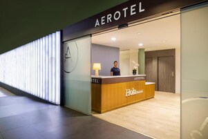 Ein Empfangsbereich eines Aerotel Hotels mit einem Holzbüro, einer Rezeptionistin und einem modernen Innendesign.