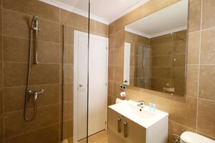 A bathroom with a shower, toilet, sink, and mirror.