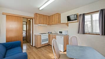 Une cuisine compacte avec des meubles en bois, un four à micro-ondes, un petit réfrigérateur et un téléviseur fixé au mur.