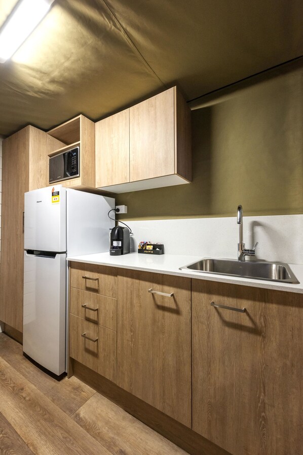 Una cocina con armarios de madera, un refrigerador blanco, un microondas, una cafetera y un lavamanos de acero inoxidable.