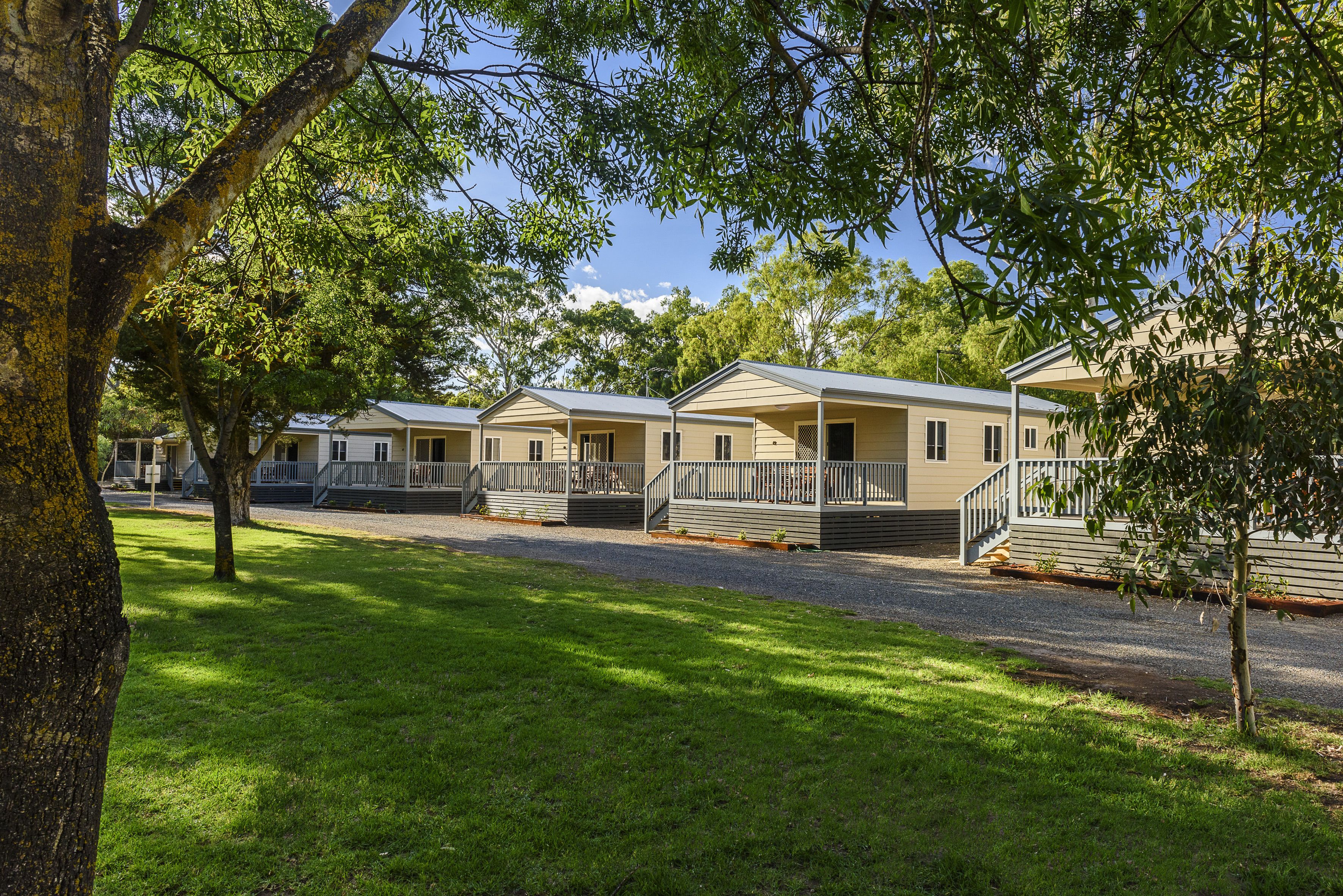 A row of single-story mobile homes with front porches and attached garages, surrounded by well-maintained lawns and trees.