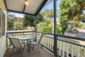 A covered outdoor area with a table and chairs, surrounded by a railing, overlooking a garden and street. - Discovery Parks - Barossa Valley (Tanunda)