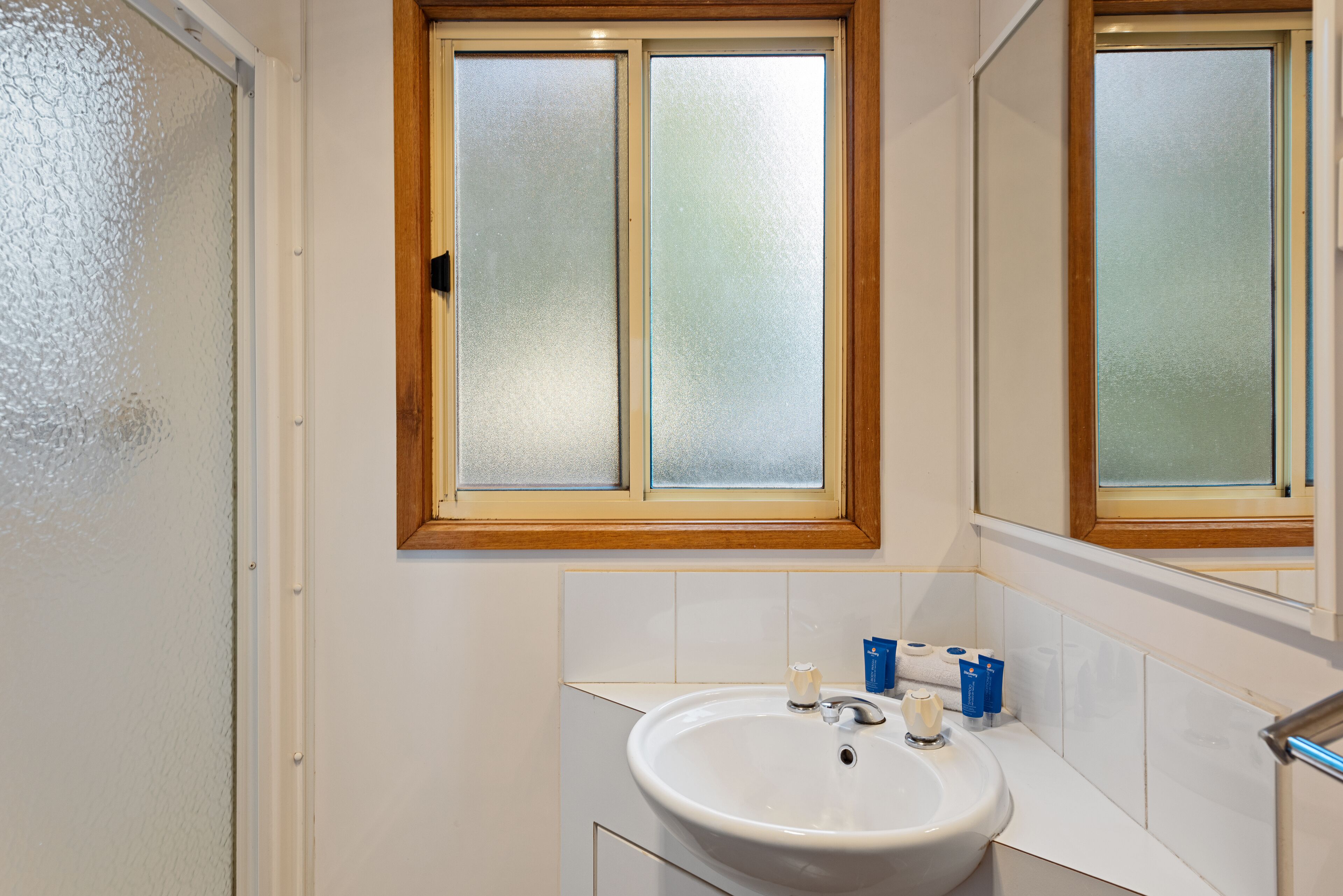 A bathroom with a white sink, a mirror, and frosted glass windows.