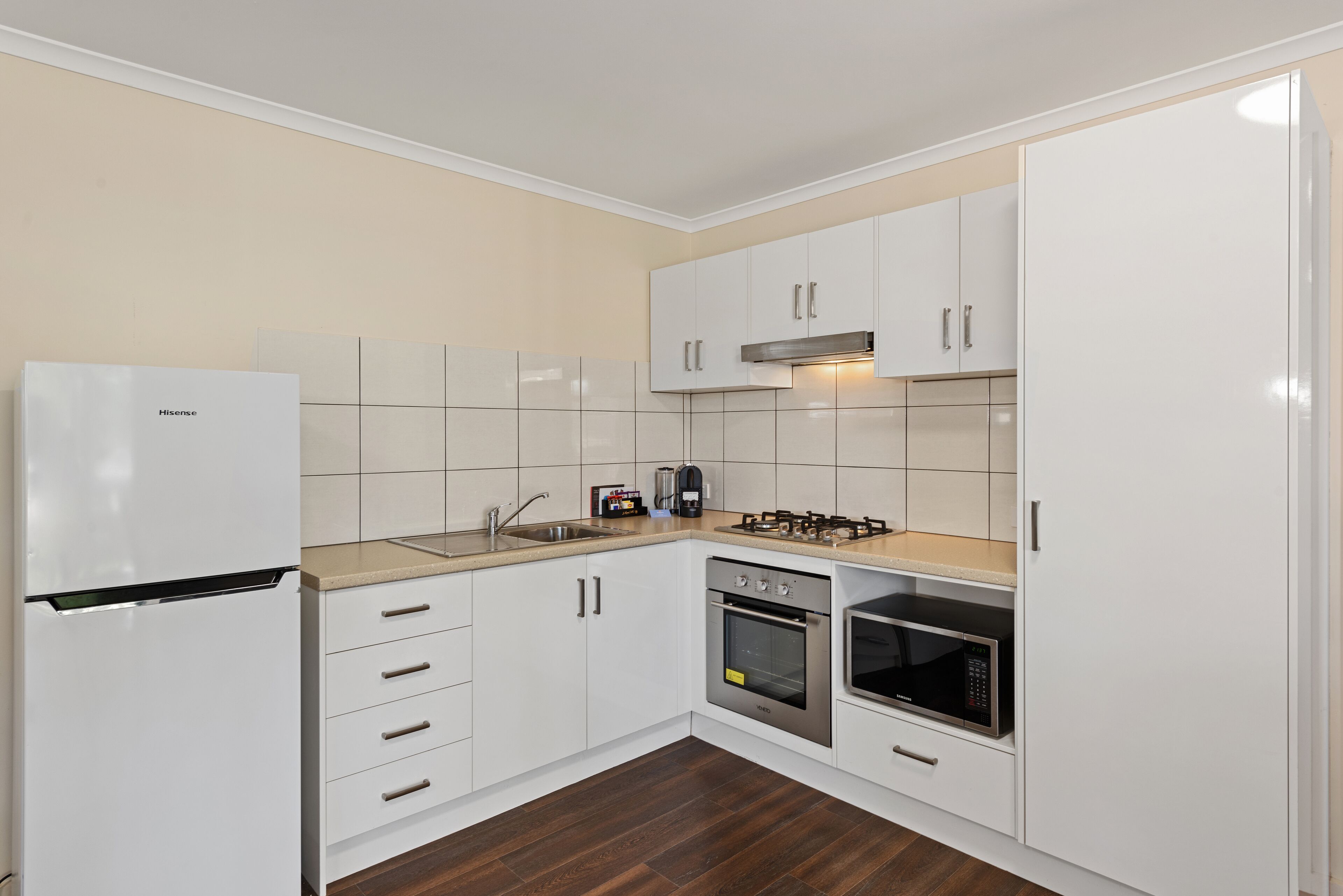 A modern kitchen with white cabinets, a stainless steel refrigerator, a gas stove, an oven, and a microwave.