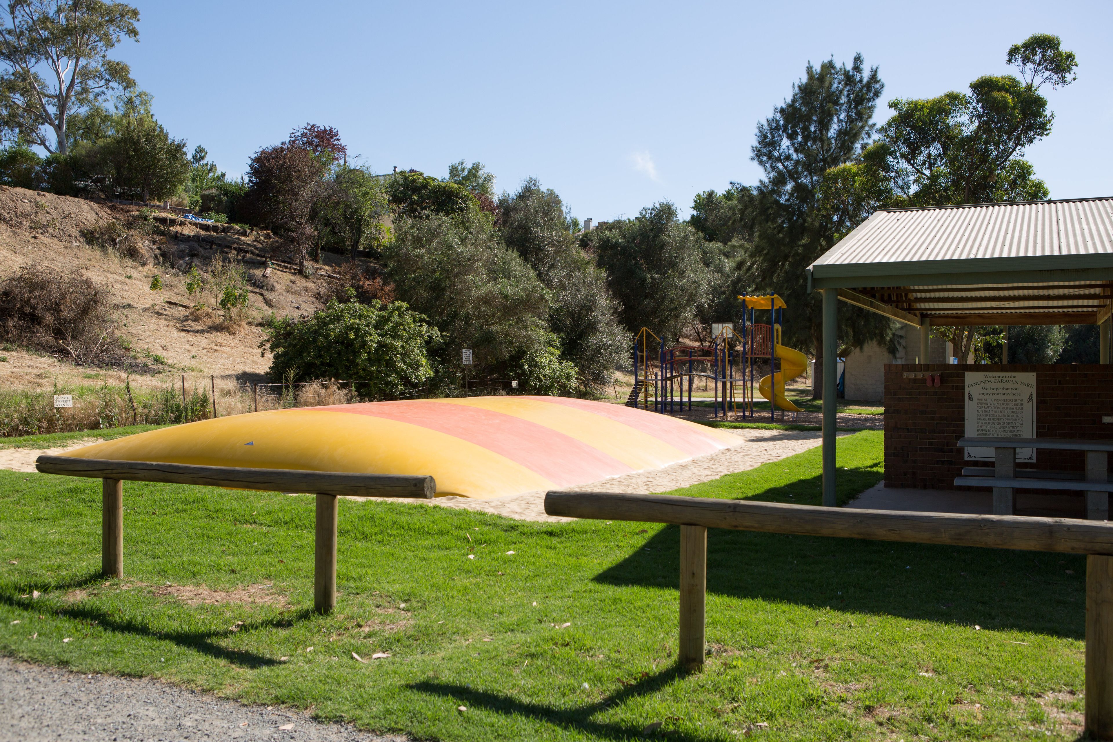 Un parque infantil con un tobogán amarillo y rojo, rodeado de césped verde y árboles.