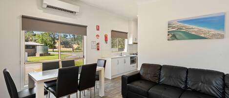 A modern living room with a black leather sofa, dining table with chairs, and a kitchen in the background.