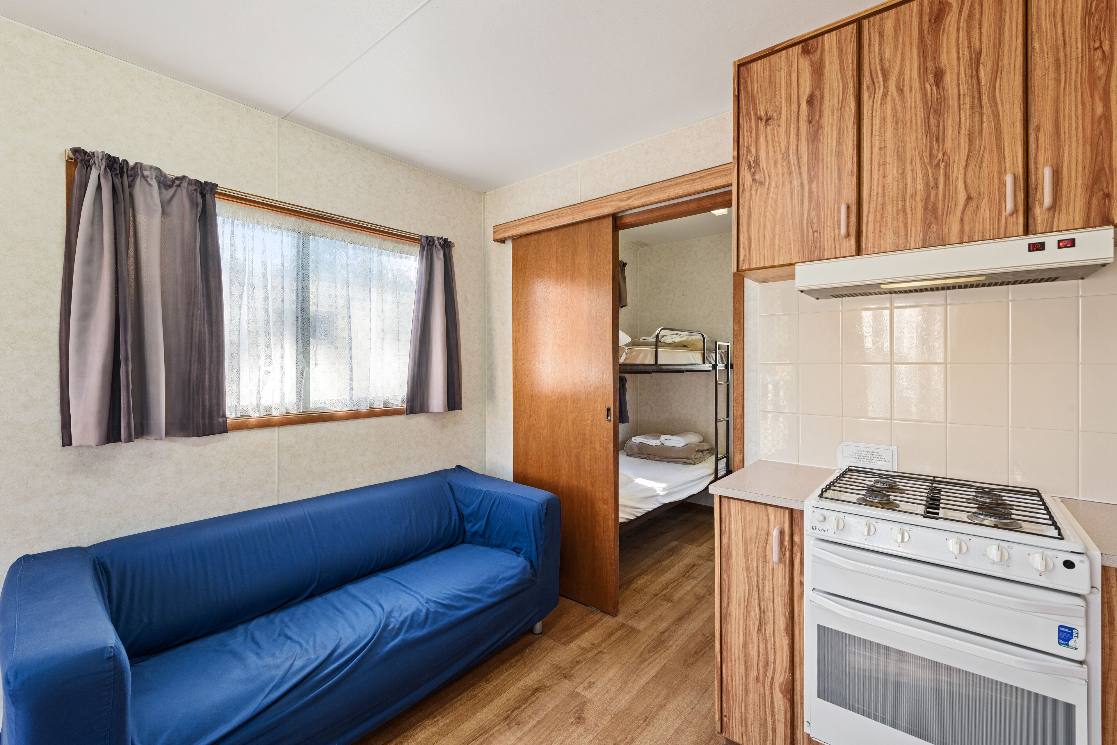 Una kitchenette compacta con estufa, armarios de madera y un sofá azul.