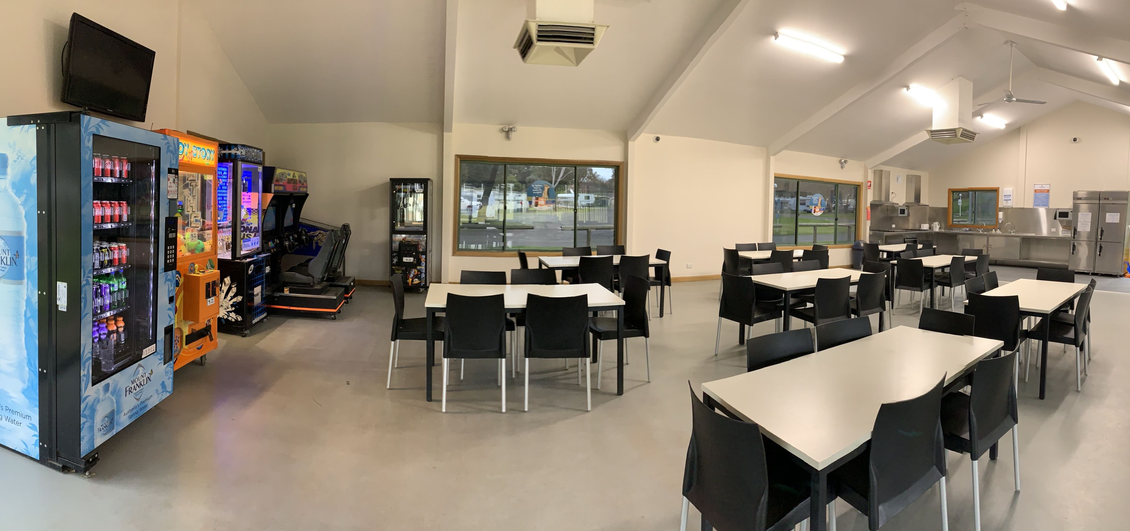 A cafeteria with tables and chairs, vending machines, and a large window.