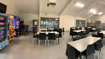 A cafeteria with tables and chairs, vending machines, and a large window.