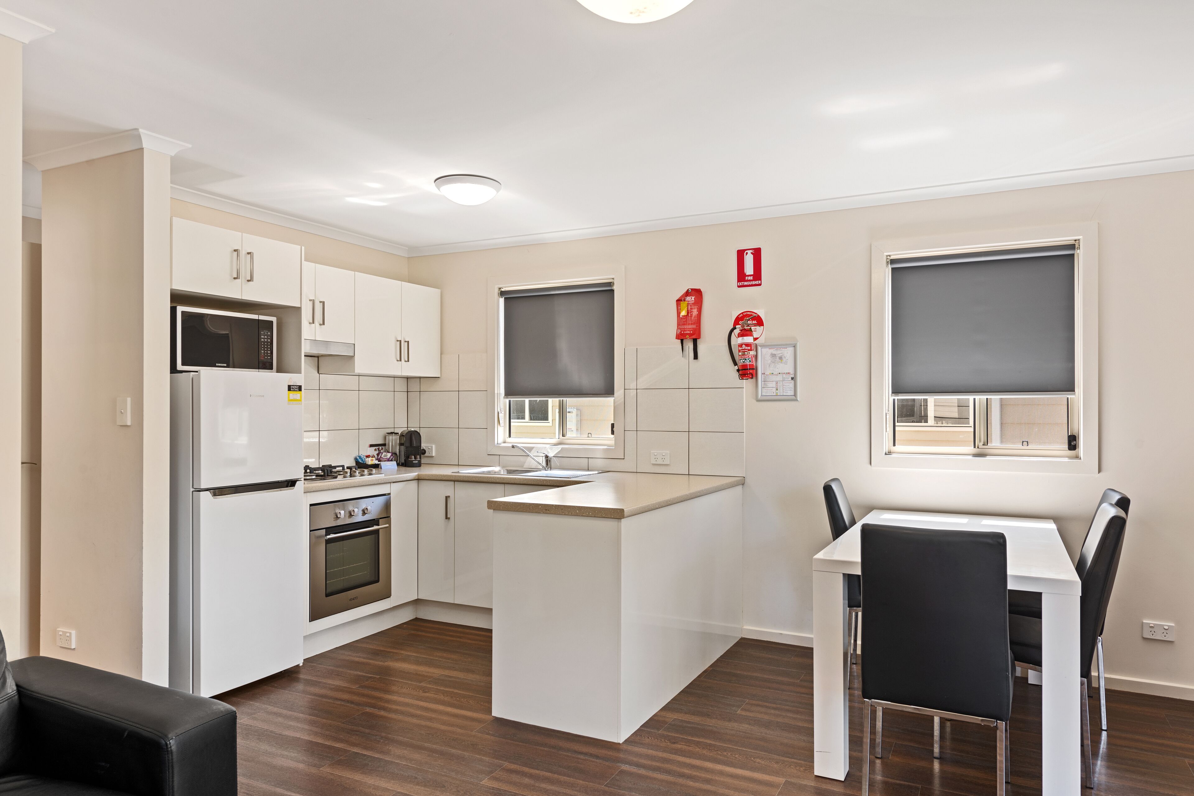 A modern kitchen with white cabinets, a built-in oven, a microwave, and a dining area with a table and chairs.