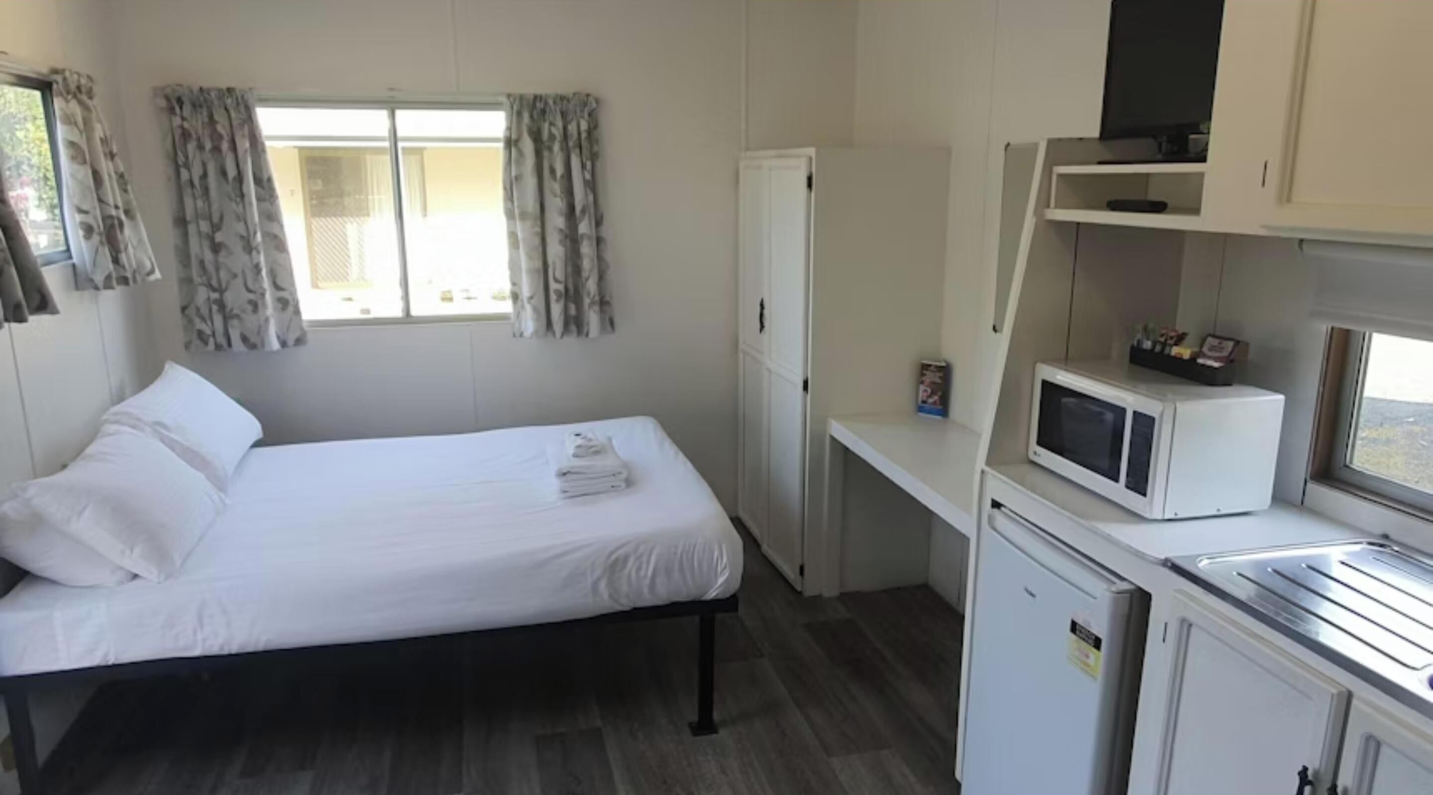 A compact room with a bed, a small kitchenette, a microwave, and a refrigerator.