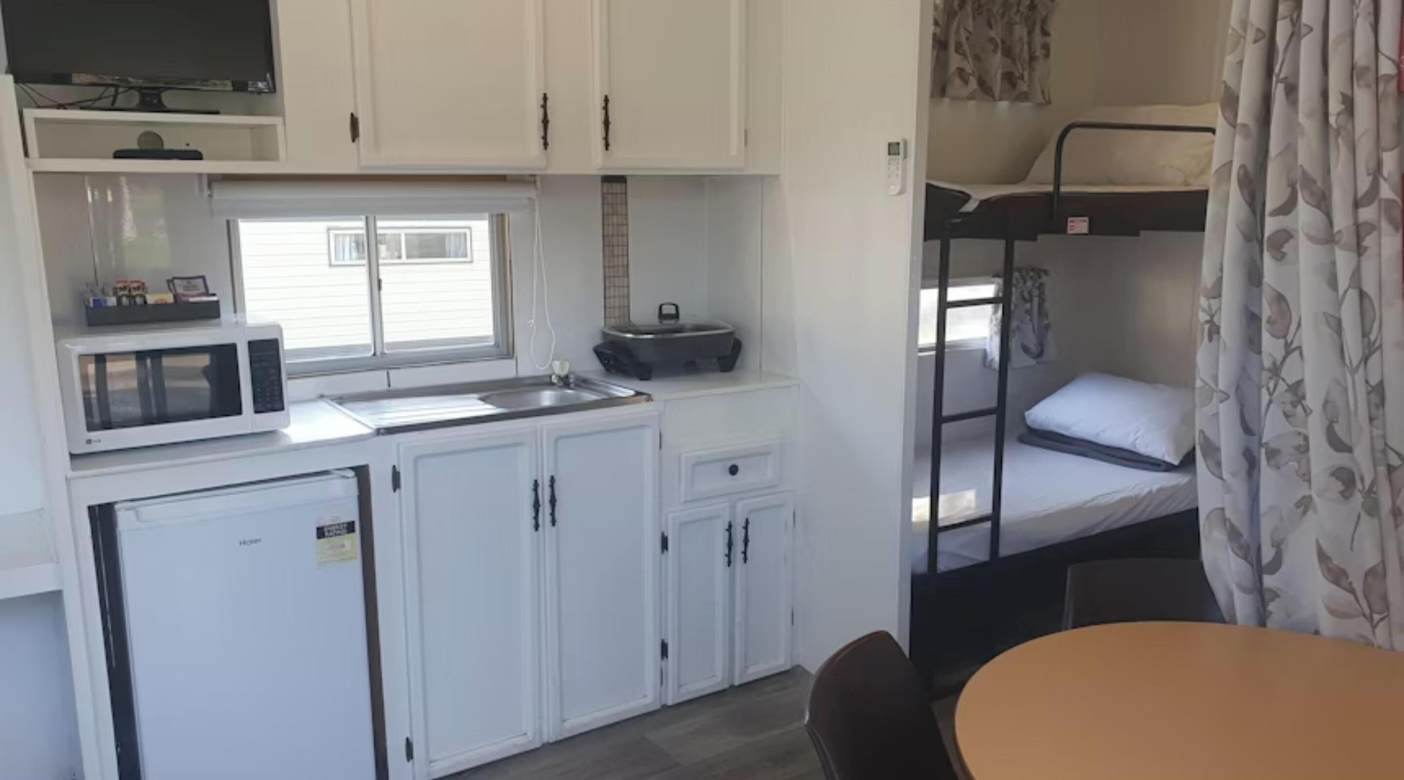 A compact kitchenette with a microwave, a small refrigerator, and a sink. There is a bunk bed with a window and a curtain.