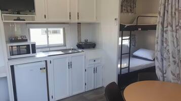 A compact kitchenette with a microwave, a small refrigerator, and a sink. There is a bunk bed with a window and a curtain.