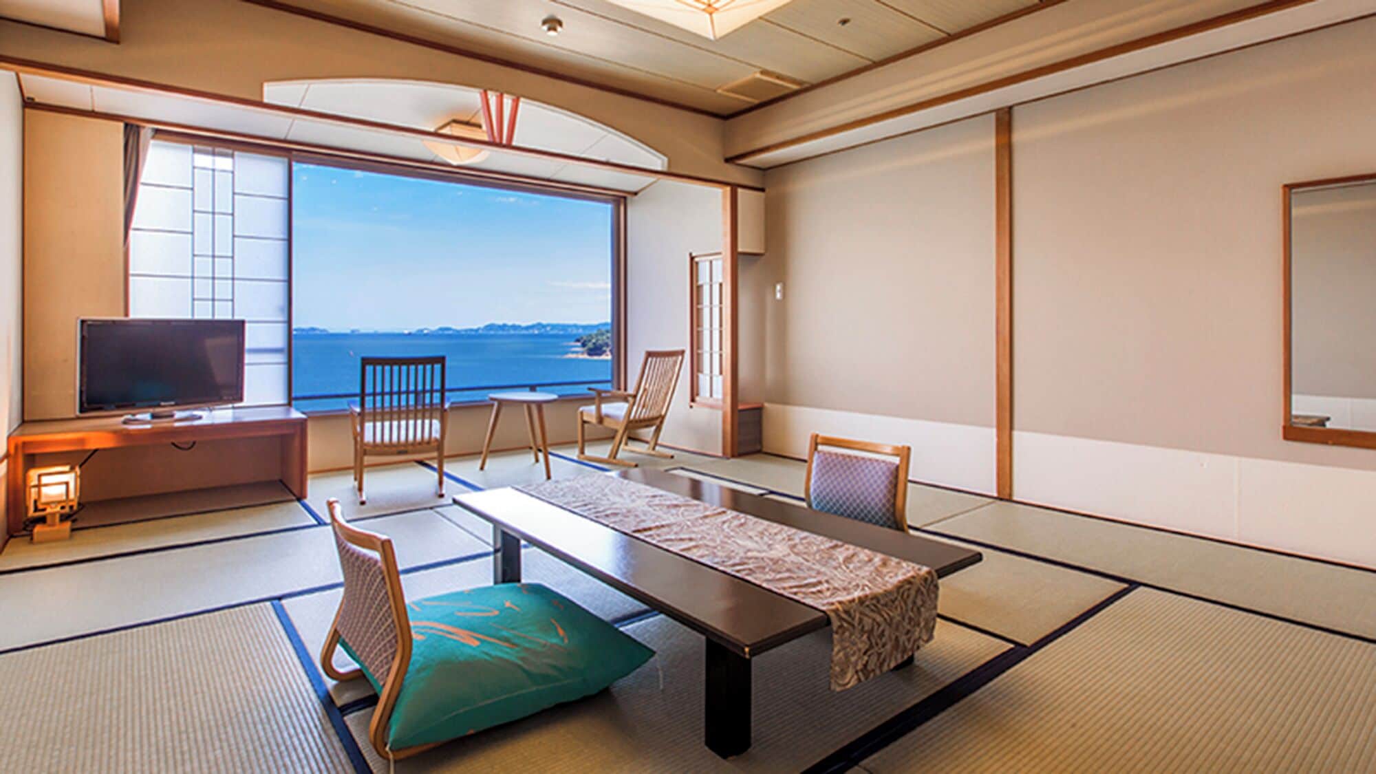 Una habitación tradicional japonesa con suelo de tatami, una mesa baja, sillas, televisión y vista al mar.