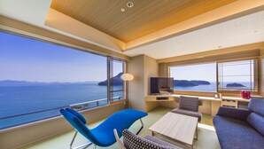 A modern room with a large window overlooking the sea, a sofa, a blue chair, and a small table. - Hotel Ofutei (Fukuyama)
