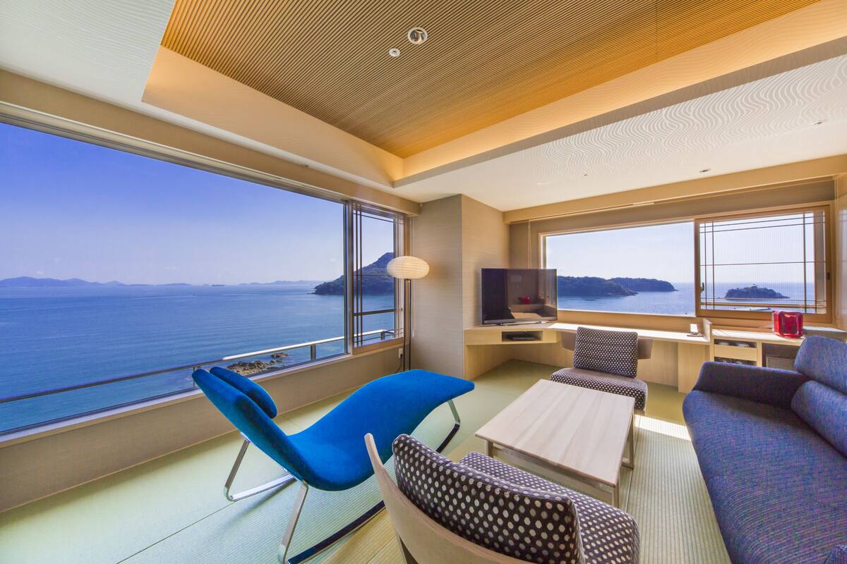A modern room with a large window overlooking the sea, a sofa, a blue chair, and a small table.