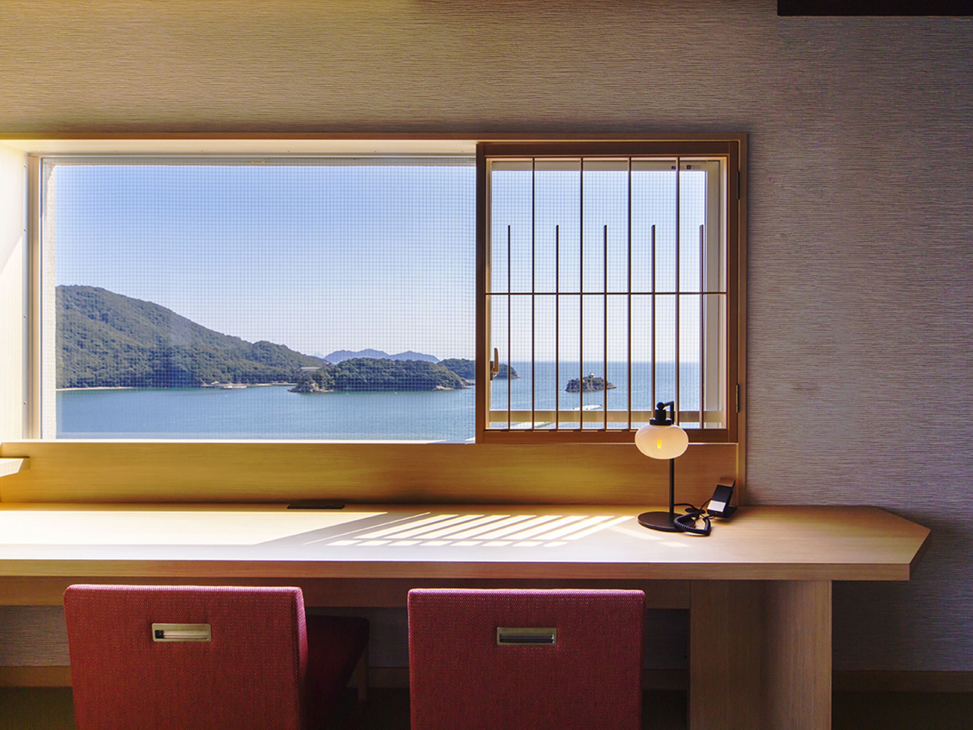 A desk with a view of a coastal landscape through a window with a grid pattern.