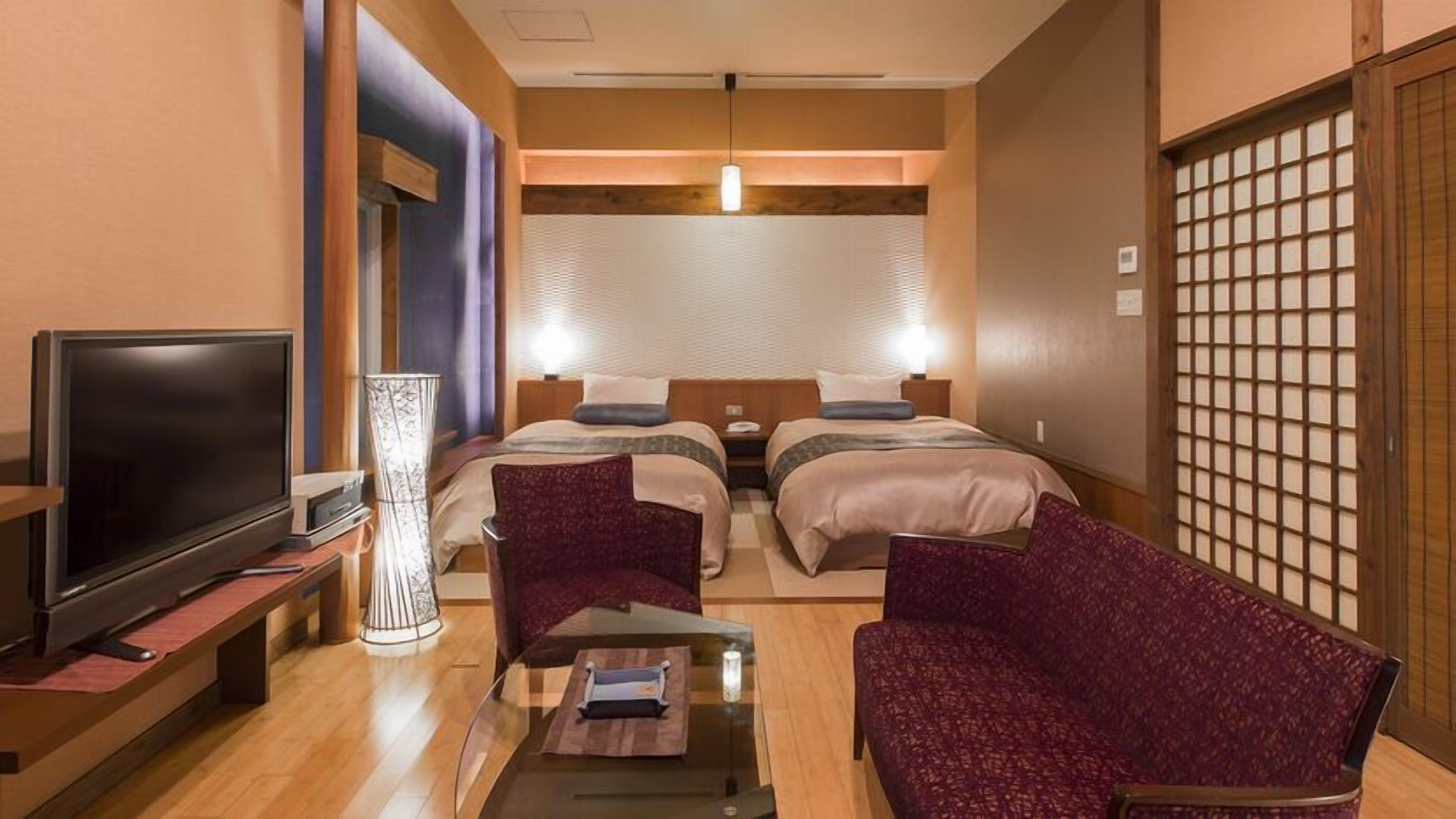 A hotel room with a TV, two beds, a desk with a lamp, and a traditional Japanese screen.