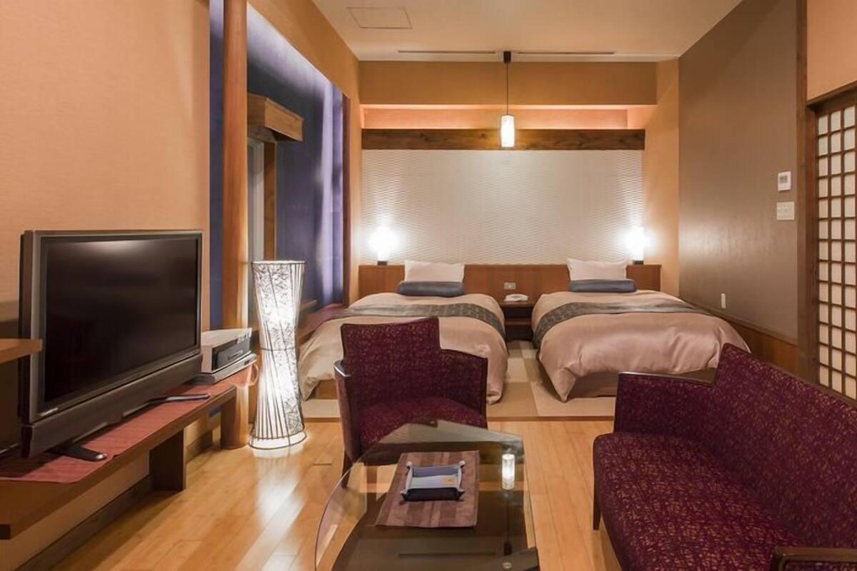 A hotel room with a TV, two beds, a desk with a lamp, and a traditional Japanese screen.