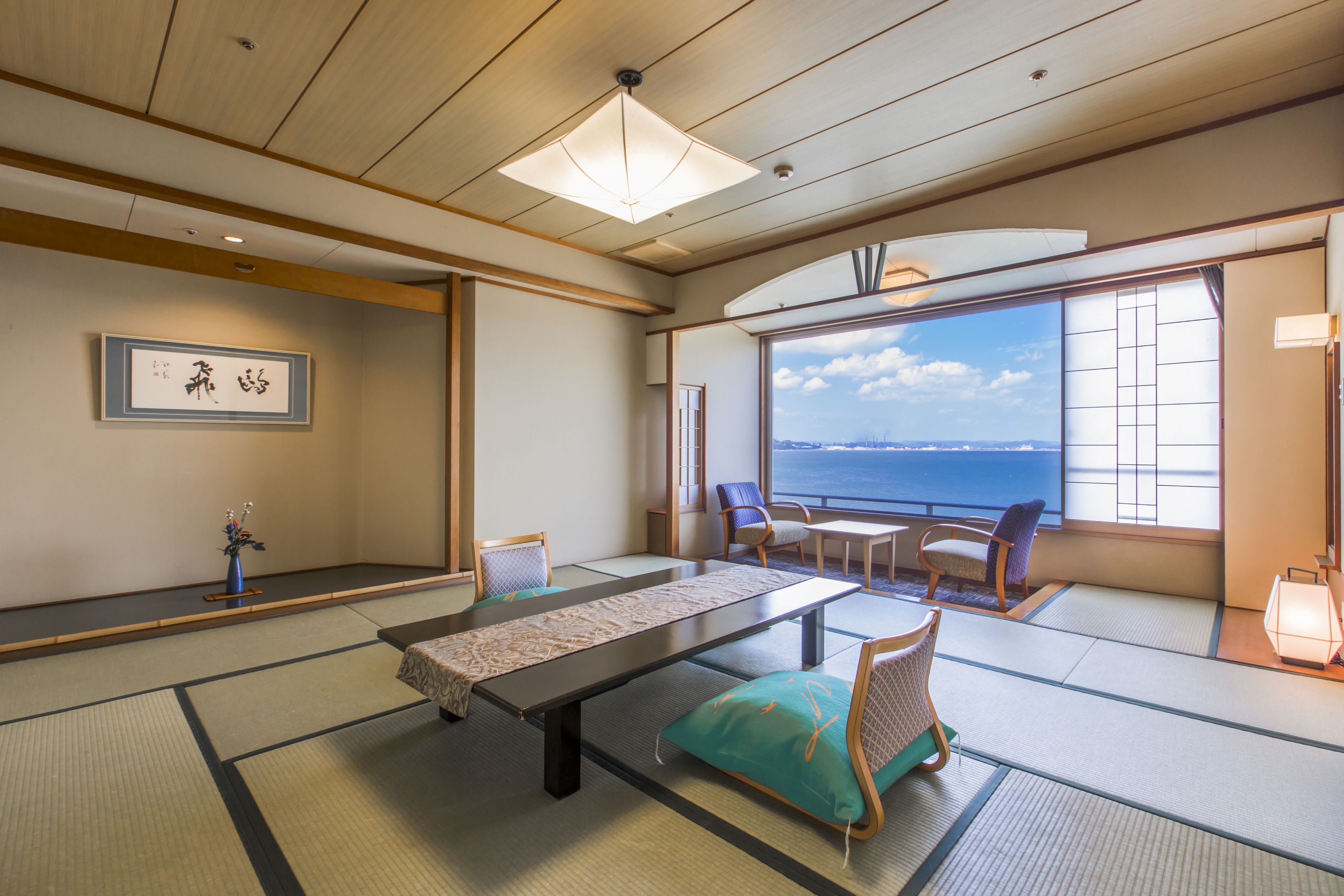 Une pièce de style japonais traditionnel, avec un sol recouvert de tatamis, une table basse, des chaises et une grande fenêtre donnant sur la mer.