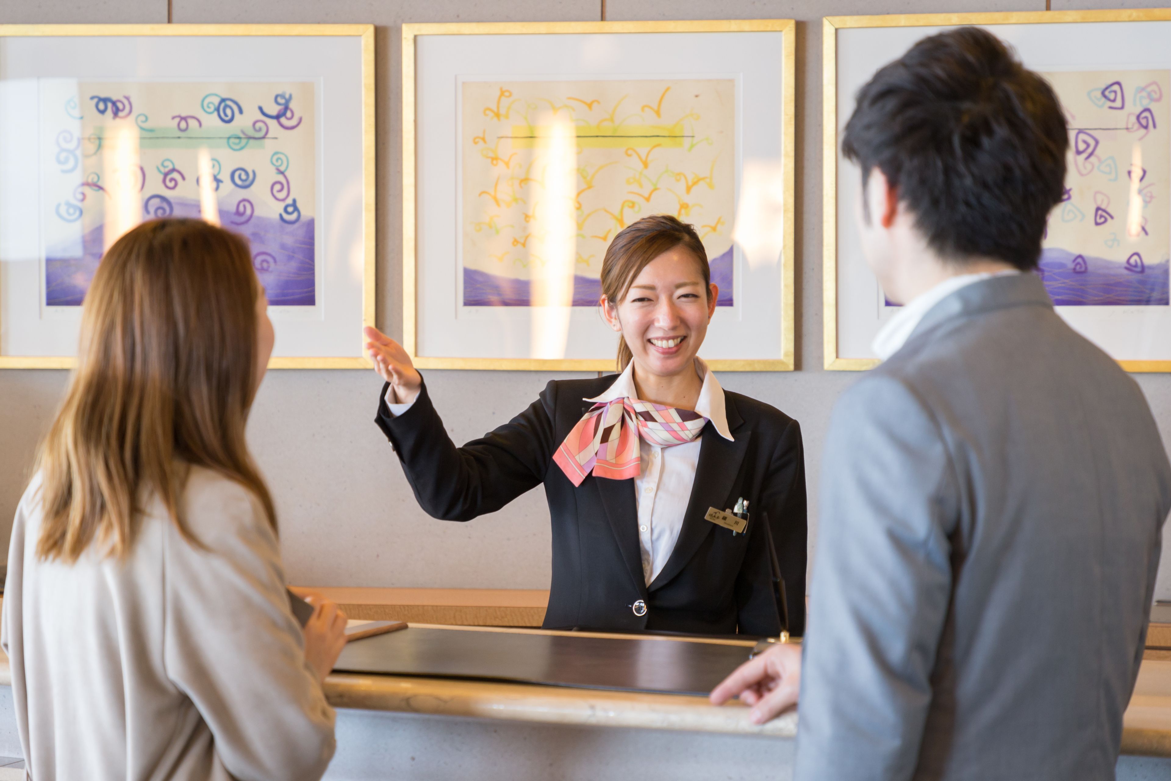 A reception desk with framed artwork on the wall, a name tag on the attendant, and a wooden counter.