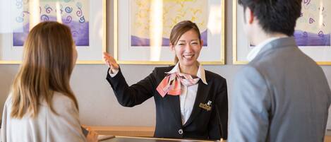 A reception desk with framed artwork on the wall, a name tag on the attendant, and a wooden counter.