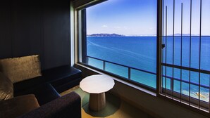 A modern room with a large window overlooking the sea, a sofa, a small round table, and a view of distant land. - Hotel Ofutei (Fukuyama)