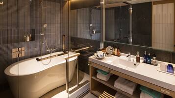 Un baño moderno con una bañera independiente, cabina de ducha con paredes de vidrio y tocador con espejo y varias botellas.