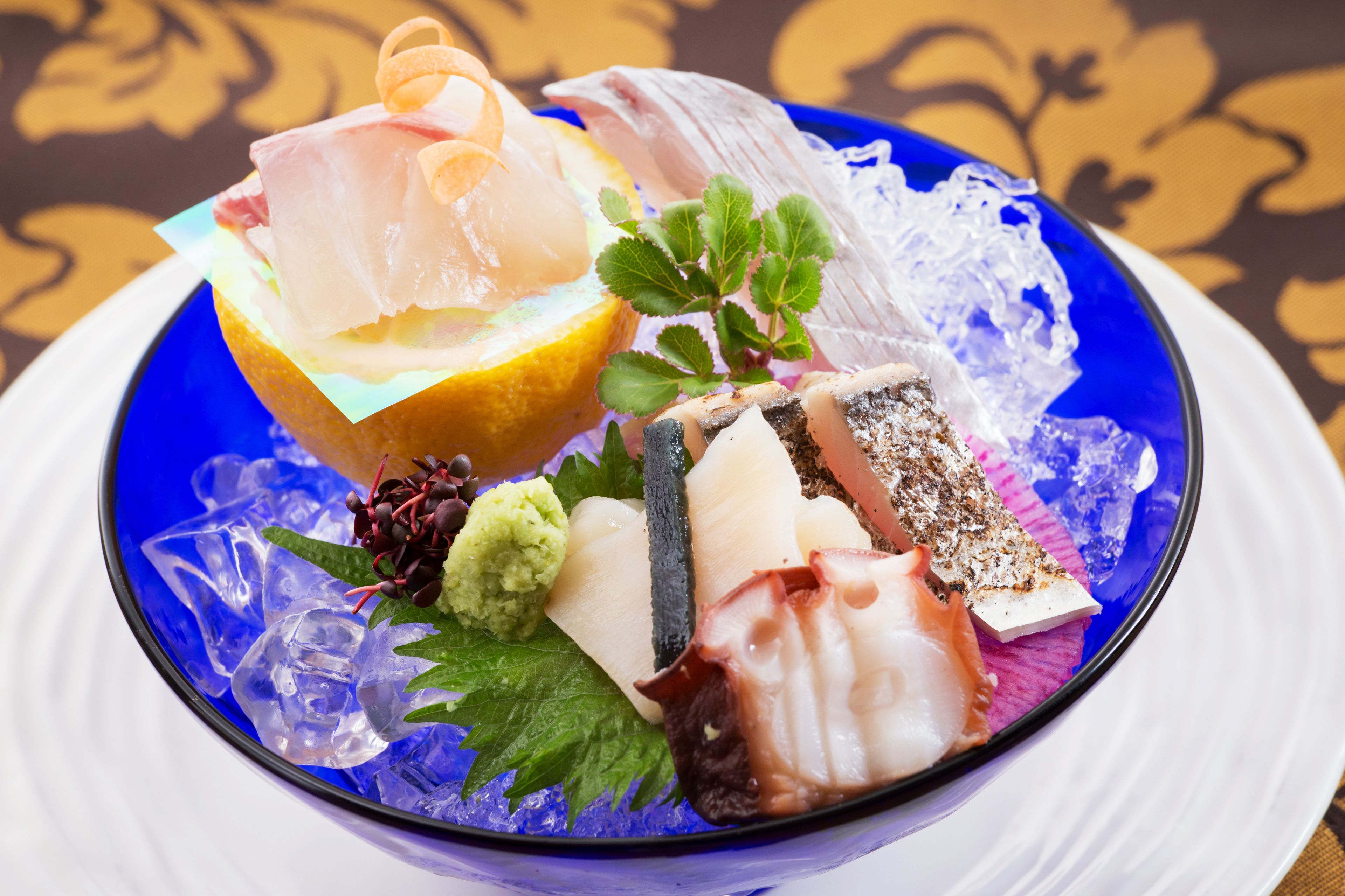 Una ciotola blu con diversi tipi di pesce e frutti di mare su un letto di ghiaccio.