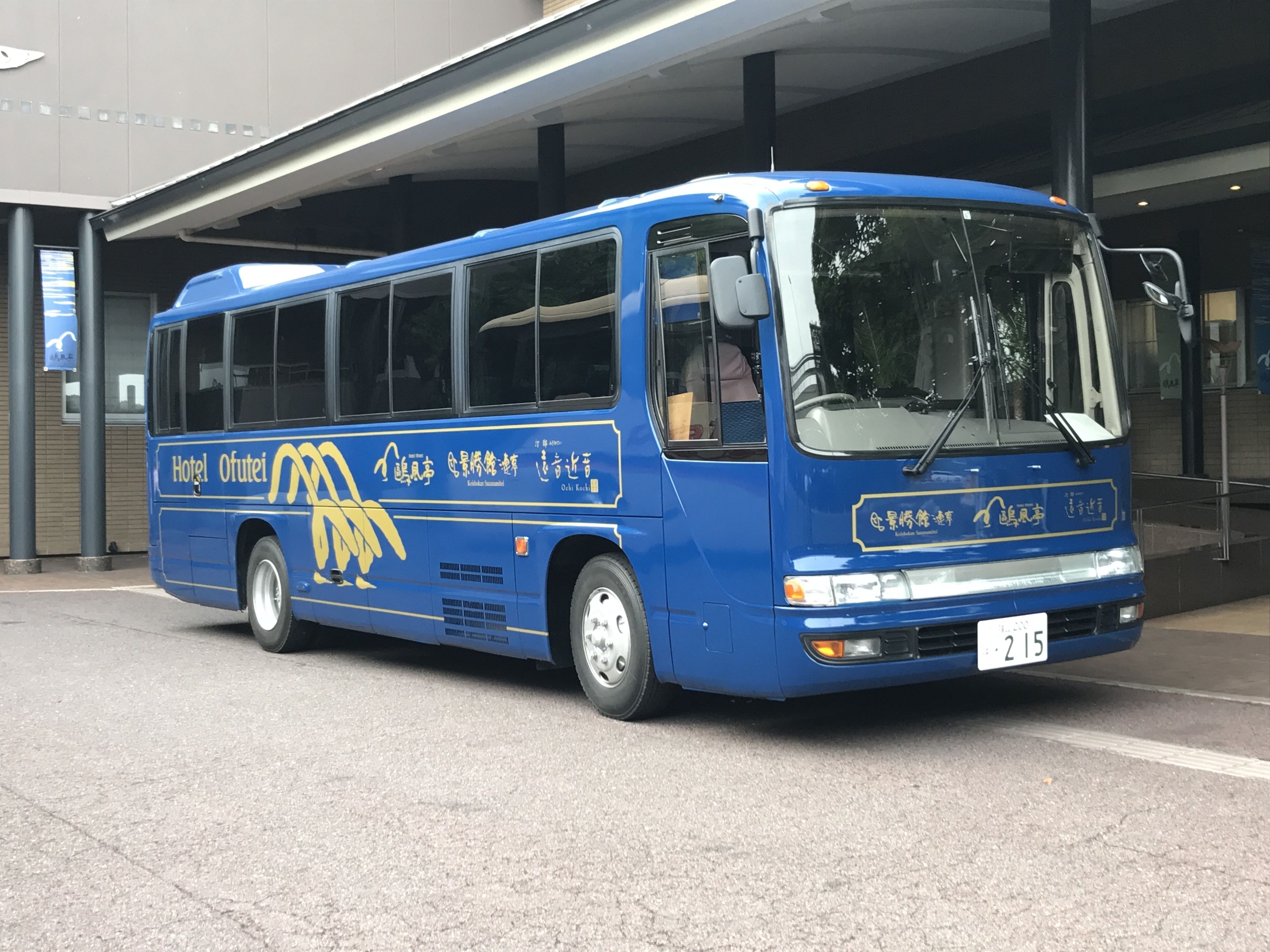 A blue bus with the text "Hotel Ofutai" and Chinese characters, parked at a bus stop.