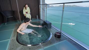 A man in a hot tub on a balcony with a view of the sea.