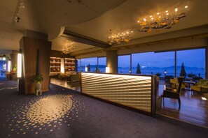 A modern hotel lobby with a large seating area, a reception desk, and a view of the mountains. - Hotel Ofutei (Fukuyama)