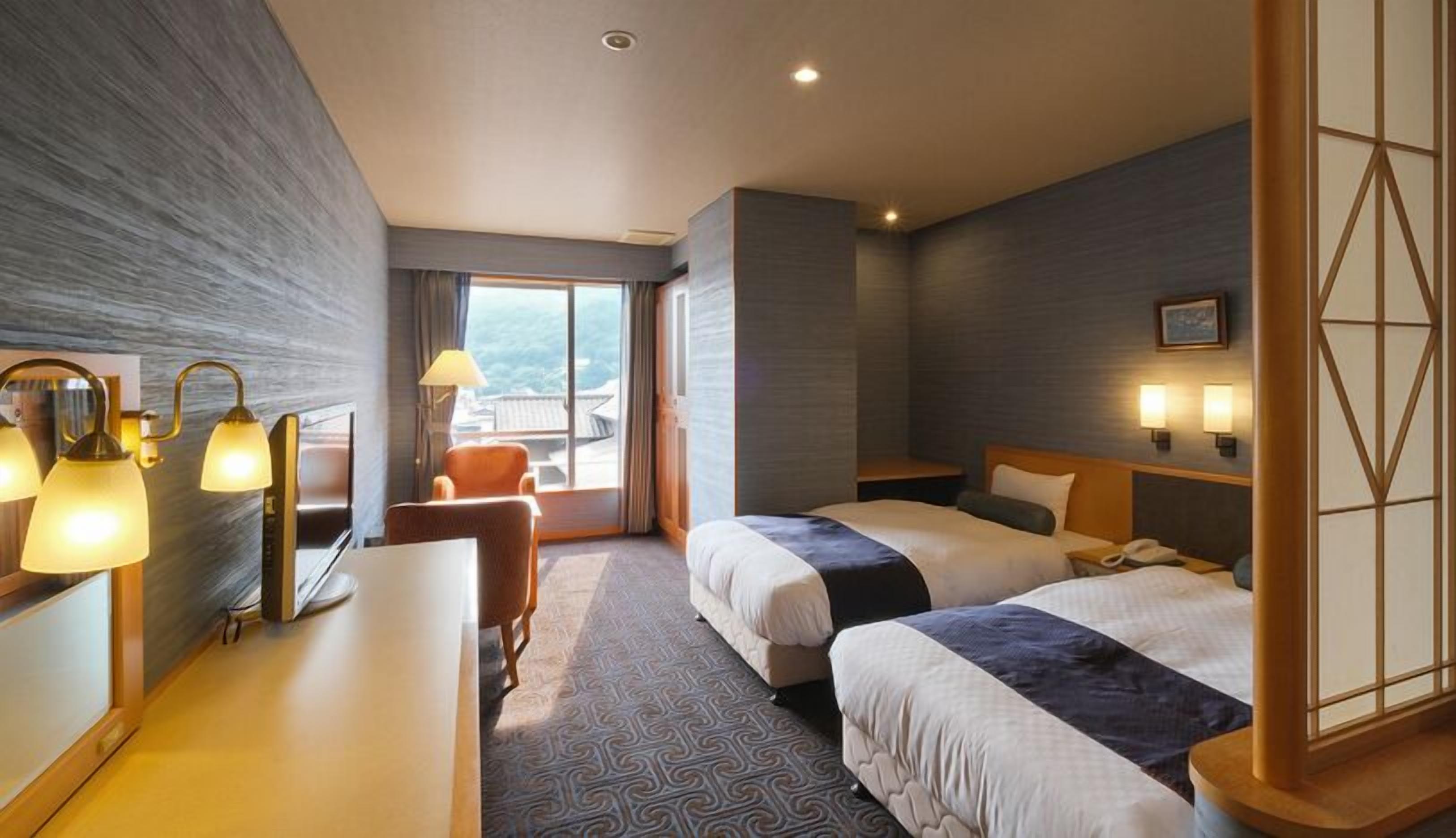 Habitación de hotel con dos camas, un escritorio, una silla y vistas al exterior.