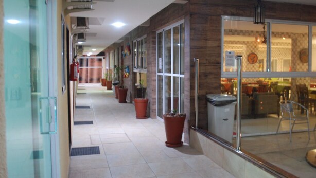 A corridor with potted plants, glass doors, and a view into a dining area. - Pousada Brasileira (Ipojuca)